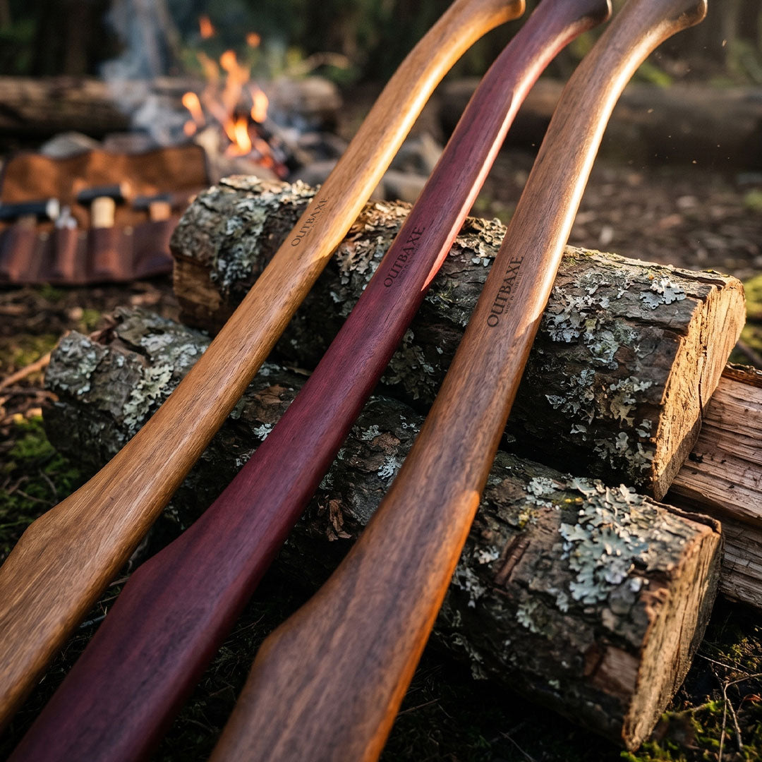Three spotted gum Outbaxe axe handles on a pile of logs with a campfire in the background